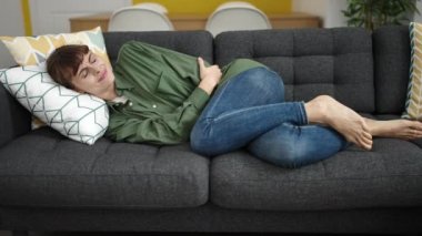 Young caucasian woman suffering from period pain lying on sofa at home