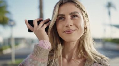 Young blonde woman smiling confident listening audio message by the smartphone at street