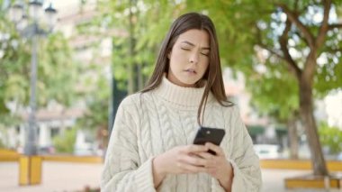 Genç, güzel, İspanyol bir kadın parkta akıllı telefon kullanıyor.