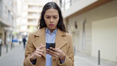 Genç ve güzel bir İspanyol kadın sokakta ciddi yüzlü akıllı telefon kullanıyor.