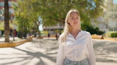 Parkta kendine güvenen genç sarışın kadın gülümsüyor.