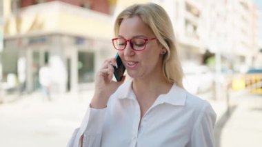 Genç sarışın kadın gülümsüyor. Kendine güveni tam. Akıllı telefondan konuşuyor.