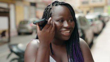 Afro-Amerikalı kadın gülümsüyor. Caddedeki akıllı telefondan kendine güvenen sesli mesaj dinliyor.