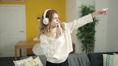 Young blonde woman listening to music and singing song at home