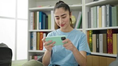 Kütüphane Üniversitesi 'nde akıllı telefondan video oyunu oynayan güzel İspanyol bir kız öğrenci.