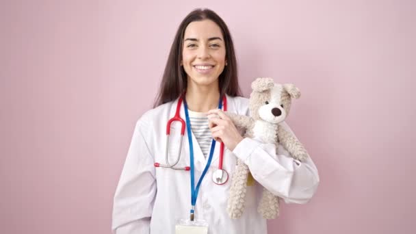 Młoda Piękna Latynoska Lekarz Trzymając Misia Robi Gest Odizolowanym Różowym — Wideo stockowe
