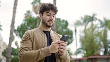 Genç İspanyol adam parkta gülümseyen akıllı telefon kullanıyor.