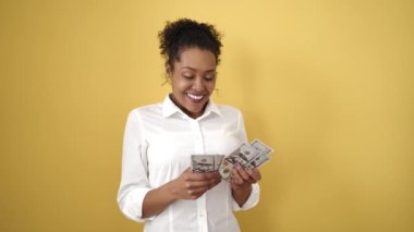 African american woman smiling confident counting dollars banknotes over isolated yellow background