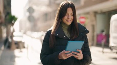 Sokakta dokunmatik ped kullanan genç İspanyol kadın gülümsüyor.