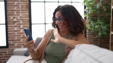 Middle age hispanic woman using smartphone and celebrating