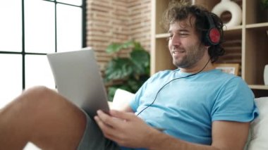 Young hispanic man having video call sitting on bed at bedroom