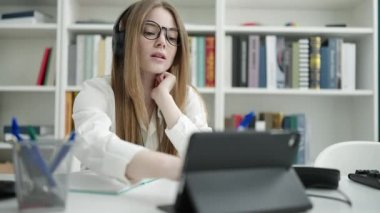 Young blonde woman student using touchpad writing on notebook at university classroom