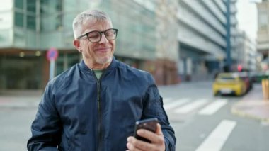 Middle age grey-haired man smiling confident having video call at street