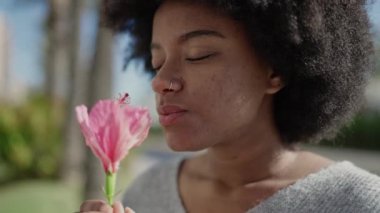 African american woman smiling confident smelling flower at park
