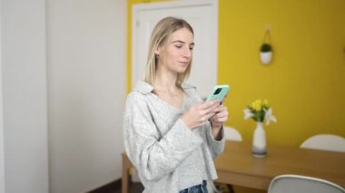 Young blonde woman using smartphone lying on the sofa at home