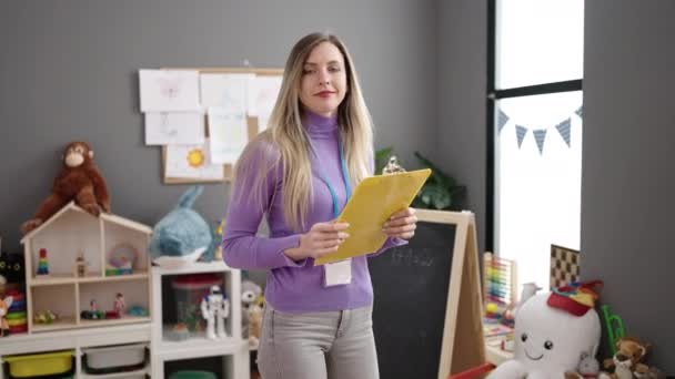 Junge Blonde Kindergärtnerin Lächelt Selbstbewusst Und Hält Checkliste Kindergarten — Stockvideo