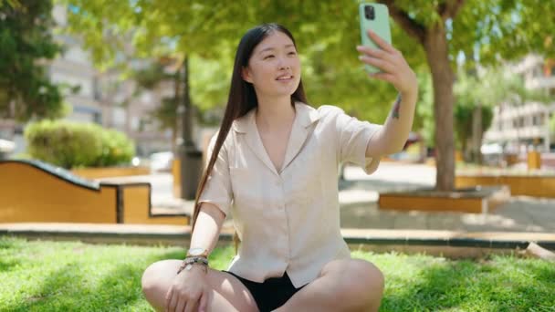 中国妇女坐在公园的草地上进行视频通话 — 图库视频影像