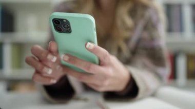 Young blonde woman student using smartphone at library university