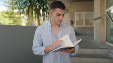 Genç İspanyol adam gülümsüyor. Sokakta kendinden emin bir şekilde kitap okuyor.