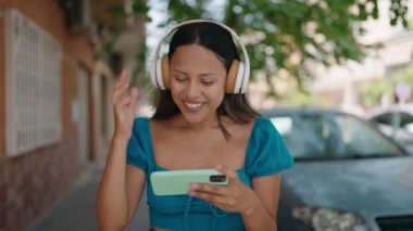 Young hispanic woman smiling confident watching video on smartphone at street