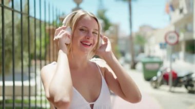 Young blonde woman smiling confident listening to music and dancing at street