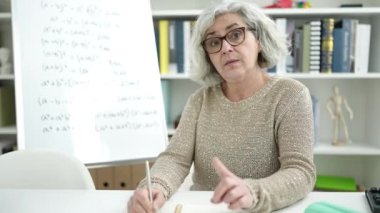 Middle age woman with grey hair teacher teaching maths lesson at university classroom