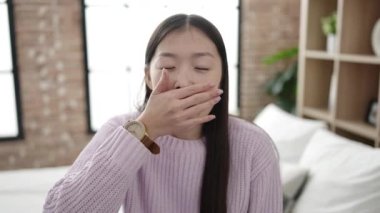 Young chinese woman waking up stretching arms at bedroom