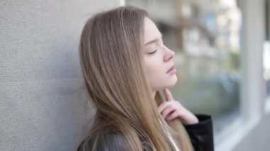 Sokakta ciddi bir ifadeyle yan tarafa bakan genç sarışın kadın.