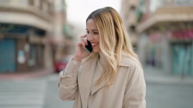 Genç sarışın kadın gülümsüyor. Kendine güveni tam. Akıllı telefondan konuşuyor.
