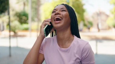Afro-Amerikalı kadın gülümsüyor. Akıllı telefondan konuşuyor.