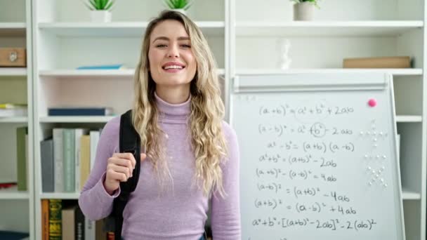 年轻的金发女学生带着自信的背包在教室里微笑 — 图库视频影像