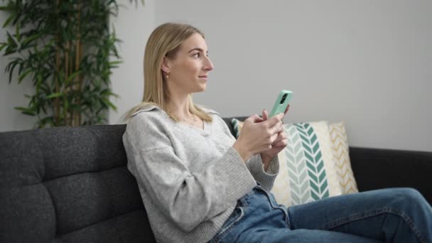 Junge Blonde Frau Sitzt Mit Smartphone Hause Auf Dem Sofa — Stockvideo