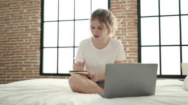 若いですブロンド女性を使用してノートパソコン書きの上にベッドルームに座って — ストック動画