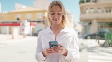 Sokakta akıllı telefon kullanan, kendine güvenen genç sarışın kadın.