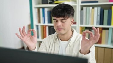 Young hispanic man student doing yoga exercise at library university