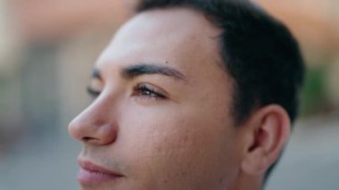 Young hispanic man looking to the sky with serious expression at street