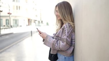 Sokakta akıllı telefon kullanan, kendine güvenen genç sarışın kadın.