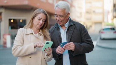 Middle age couple couple using smartphone and credit card at street