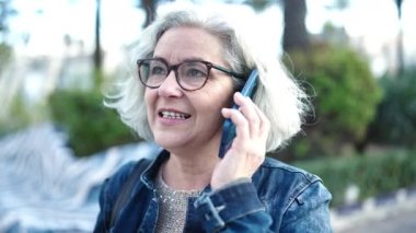 Middle age woman with grey hair speaking on the phone at park