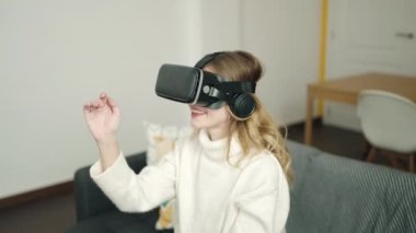 Evde sanal gerçeklik gözlüğü kullanarak video oyunu oynayan genç sarışın kadın.