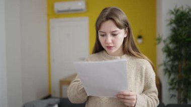 Evinde sürpriz ifadesiyle doküman okuyan genç sarışın kadın.