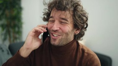 Genç İspanyol adam akıllı telefonda konuşuyor. Evdeki kanepede oturuyor.