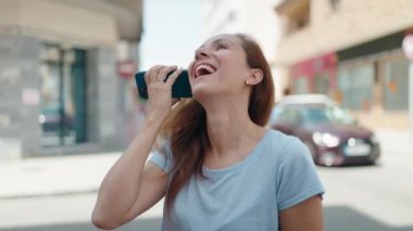 Caddedeki akıllı telefondan kendine güveni tam bir sesli mesaj dinleyen genç bir kadın.