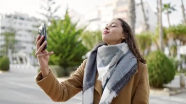 Genç ve güzel İspanyol kadın gülümsüyor. Kendine güveni tam. Sokakta akıllı telefonun yanında selfie çekiyor.