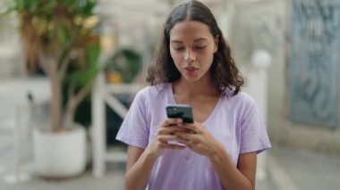 Genç Afro-Amerikalı kadın sokakta akıllı telefon kullanarak gülümsüyor.