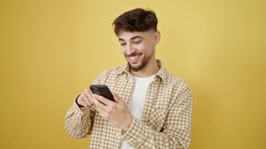 Genç Arap adam kendinden emin bir şekilde sarı arka plan üzerinde akıllı telefon kullanıyor.