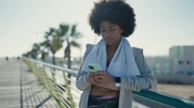 Afro-Amerikalı kadın spor giyer, sokakta akıllı telefon kullanır.