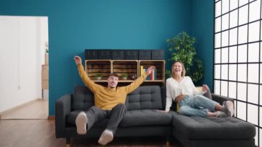 Genç çift gülümsüyor evdeki kanepede rahatlıyor.