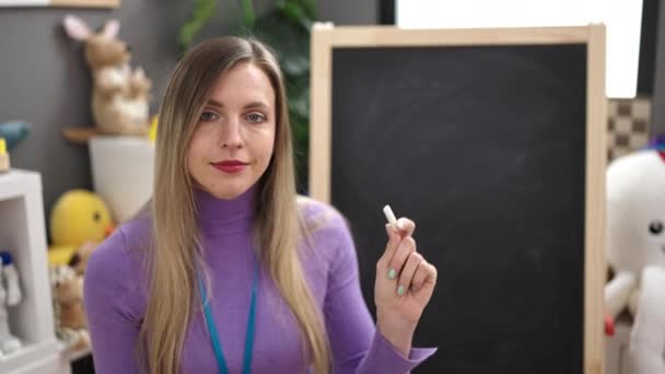 Młoda Blondynka Kobieta Przedszkolanka Nauczyciel Uśmiecha Się Pewnie Trzymając Kredę — Wideo stockowe