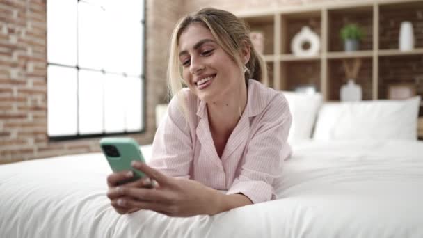 年轻的金发女人用智能手机躺在床上 — 图库视频影像